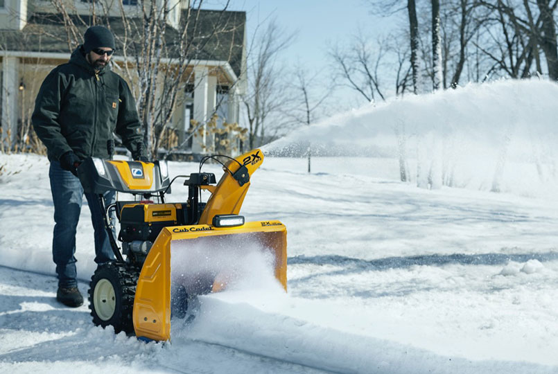 Man using cub cadet two stage snow blower to clear drive