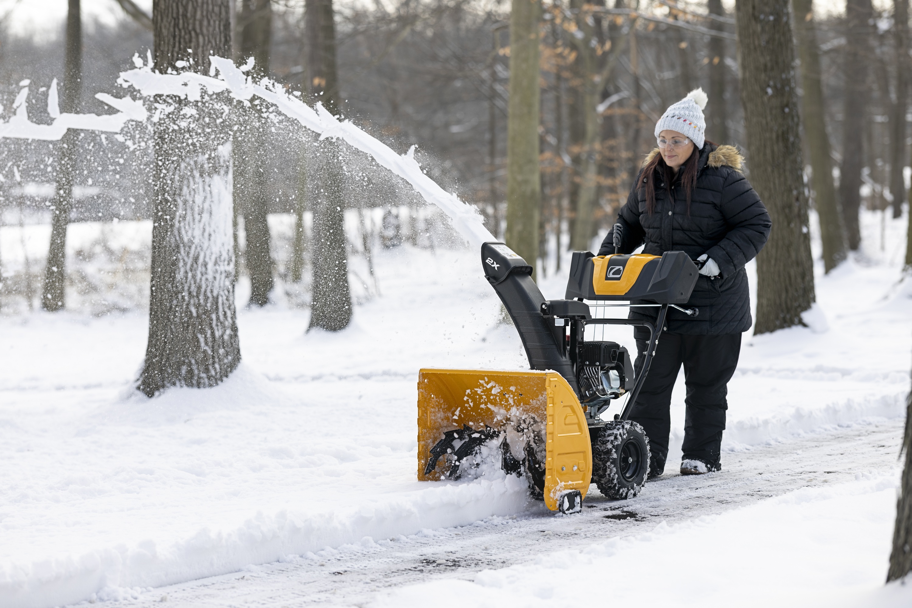 Cub Cadet® 2X® snow blower Cub Cadet® 2X® snow blower clearing snow from a residential driveway with trees in the background