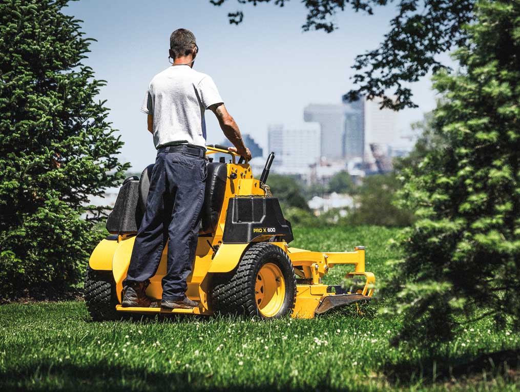 man cutting the grass between pines trees with a commercial stand-on mower