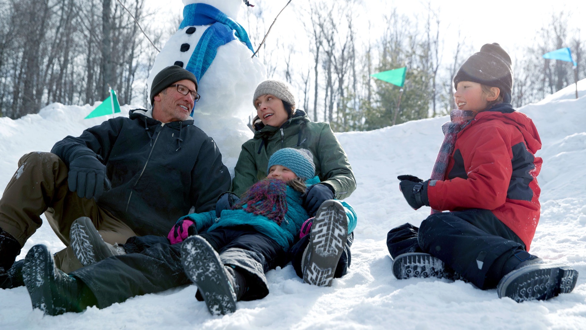 family sitting outdoors sitting in snow with snowman in background