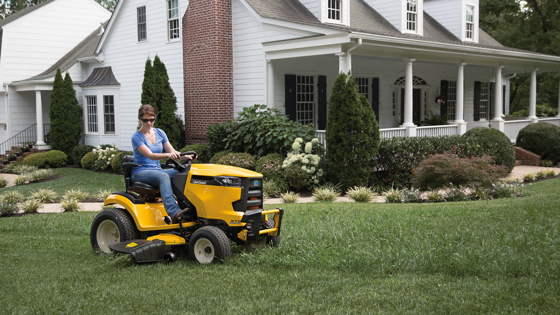 woman mowing her front yard with a lawn tractor
