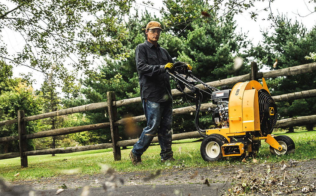 man using commercial blower to blow leaves off pavement