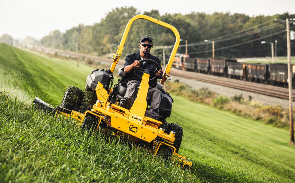 man driving commercial zero turn mower on a slope of a hill